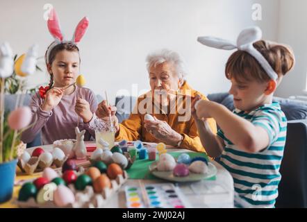 Großmutter mit kleinen Kindern, die ostereier zu Hause dekorieren. Tradition der Eiermalerei mit Pinsel und ostereifarbe. Stockfoto