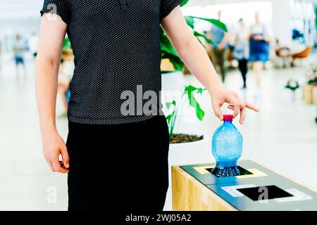 Schließen Sie die Hand, werfen Sie leere Plastikwasserflasche in den Recyclingbehälter, und recyceln Sie den Abfall Stockfoto