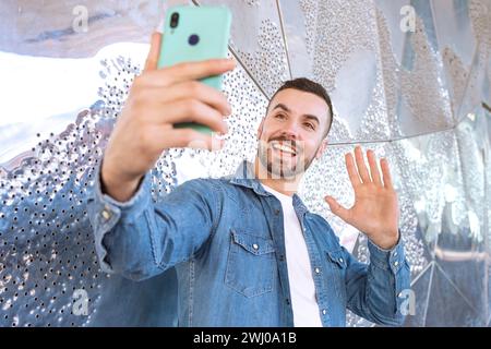 Ein lächelnder junger Mann, der draußen mit einem Smartphone telefoniert. Stockfoto