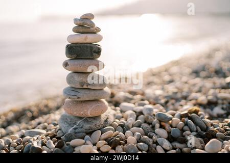 Eine Steinpyramide steht an einem Kiesstrand in der Nähe des Meeres, das in der Sonne glitzert Stockfoto