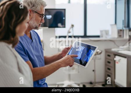 Arzt zeigt weiblichen Patienten MRT-Scan auf Tablette und bespricht Testergebnis in der Notaufnahme. Stockfoto