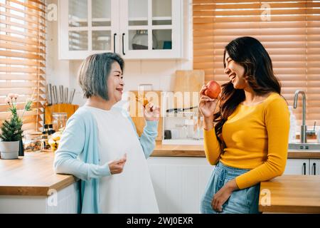 Eine ältere Mutter und ihre erwachsene Tochter, eine junge Frau in einer Schürze, verbinden sich mit Essen in der Küche Stockfoto