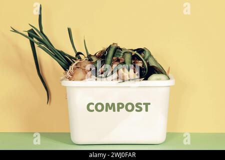 Kompostierkorb in der Küche. Geschältes Gemüse in weißem Kompostbehälter auf mehrfarbigem Hintergrund. Papierkorb Stockfoto