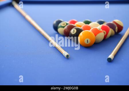 Billard-Kugeln und Billard-Queue sind an einem sonnigen Sommertag im Freien auf dem blauen Billard-Tisch. Queue auf dem Tisch, kurz vor dem Ball, Bokeh-Foto Stockfoto