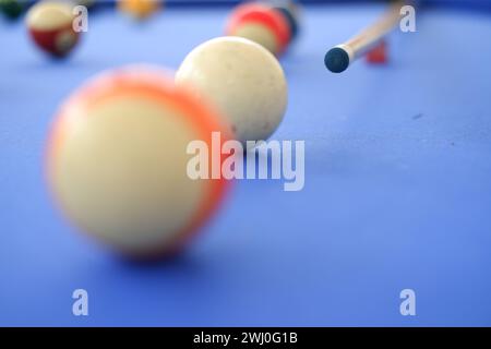 Billard-Kugeln und Billard-Queue sind an einem sonnigen Sommertag im Freien auf dem blauen Billard-Tisch. Queue auf dem Tisch, kurz vor dem Ball, Bokeh-Foto Stockfoto