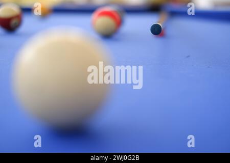 Billard-Kugeln und Billard-Queue sind an einem sonnigen Sommertag im Freien auf dem blauen Billard-Tisch. Queue auf dem Tisch, kurz vor dem Ball, Bokeh-Foto Stockfoto