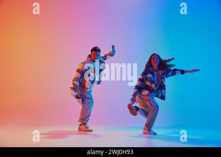 Porträt von Hip-Hop-Tänzern in voller Länge, die in Bewegung vor dem Hintergrund des Gradienten-Studios auftreten. Synchronisierte Bewegungen. Stockfoto