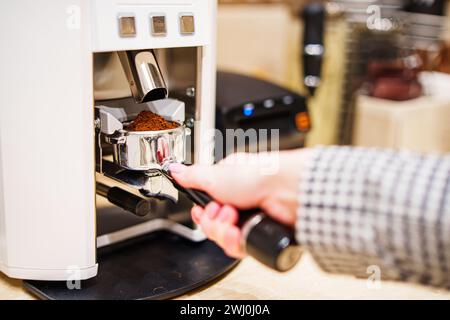 Ausstattung der Kaffeemaschine, der mit fein gemahlenem Kaffee gefüllte Portafilter in den Händen des Barista, der sich auf die Zubereitung von Kaffee vorbereitet. Stockfoto