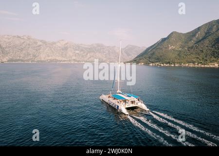 Ein großer Segelkatamaran für Passagiere schwimmt auf dem Meer entlang der Berge. Drohne Stockfoto