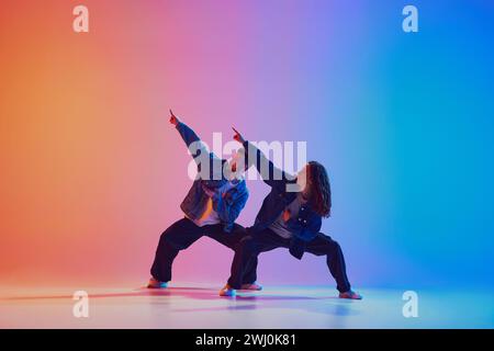Dynamische Aufnahme junger, athletischer Tänzerinnen und Tänzerinnen in modernen Denim-Outfits, die in Bewegung vor einem Hintergrund in Neon tanzen Stockfoto