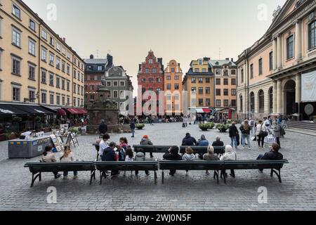 Eine Straßenszene mit Leuten, die auf Bänken vor bunten Gebäuden sitzen. Stockholm Stockfoto