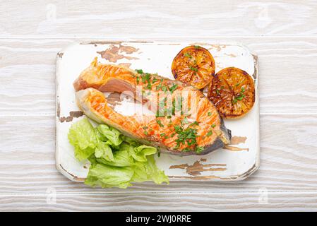 Gegrilltes Fisch Lachssteak und grüner Salat mit Zitrone serviert auf weißem Schneidebrett rustikaler Holzhintergrund mit Blick von oben, ausgewogene d Stockfoto