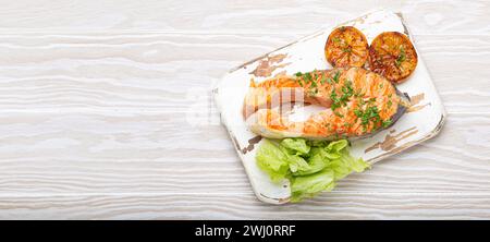 Gegrilltes Fisch Lachssteak und grüner Salat mit Zitrone serviert auf weißem Schneidebrett rustikaler Holzhintergrund mit Blick von oben, ausgewogene d Stockfoto