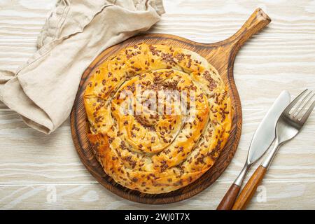 Bürek aus Filoteig mit Füllung auf Schneidebrett, weißer hölzerner rustikaler Hintergrund von oben. Traditioneller herzhafter Spiralkuchen Stockfoto