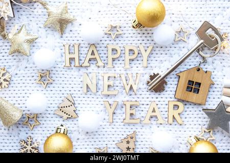 Hausschlüssel mit Schlüsselanhänger auf festlichem gestricktem Hintergrund mit Sternen, Lichtern von Girlanden. Frohe Neujahrsbriefe aus Holz, gre Stockfoto