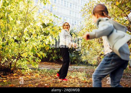 Frau mittleren Alters in lässiger Kleidung und ihre kleine süße Enkelin spielt Spiel im Herbst Park. Lächelnde Großmutter und süß Stockfoto