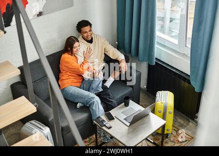 Junges multiethnisches Paar, das einen ruhigen Moment auf einem gemütlichen Sofa mit Laptop in einem modernen Hostel genießt Stockfoto