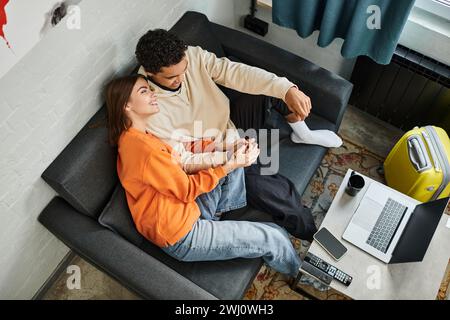 Intime Überkopfaufnahme eines interrassischen Paares, das auf einem Sofa liegt und gemeinsam auf einem Laptop einen Film ansieht Stockfoto