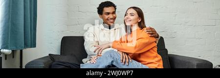 Fröhliches, abwechslungsreiches Paar genießt gemütliche Momente auf einem Sofa im Hostel, Reise- und Komfortkonzept Stockfoto