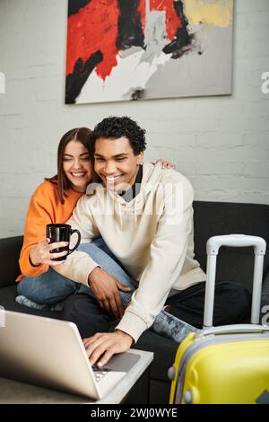 Das aufregende interrassische Paar teilt sich einen gemütlichen Moment, während es auf der Couch sitzt und ein Notebook benutzt Stockfoto