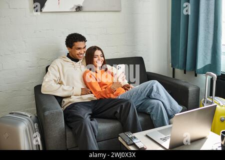 Glückliche, vielfältige Paare teilen sich einen gemütlichen Moment, indem sie auf einer bequemen Couch durch die Telefone scrollen Stockfoto