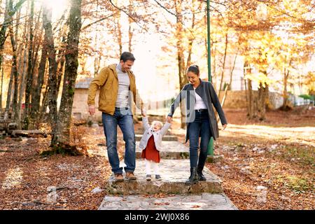 Das kleine Mädchen steht auf einem gepflasterten Weg im Park und hält Hände mit Mom und Dad Stockfoto