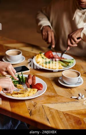 Junges, vielfältiges Paar, das Frühstück im Café genießt, Omelette und Würstchen in der Nähe einer Tasse Kaffee Stockfoto