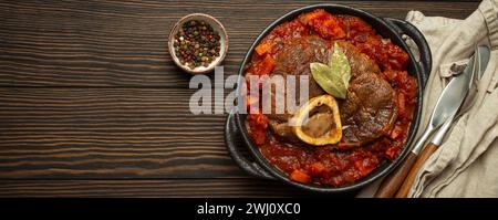 Traditionelles italienisches Gericht Ossobuco ganz Milanese mit geschnittenem Kalbsschenkelfleisch mit Gemüsetomatensauce serviert in schwarzem cassero Stockfoto