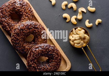 Schokoladen-Donuts, bestreut mit zerquetschten Nüssen auf einem schwarzen Tisch Stockfoto