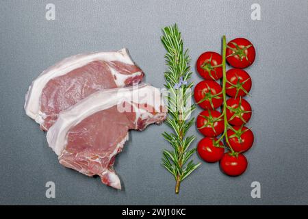 Geschnittenes rohes Schweinefleisch auf schwarzem Hintergrund. Frische Schweinekoteletts mit Rosmarin und Cocktail Stockfoto