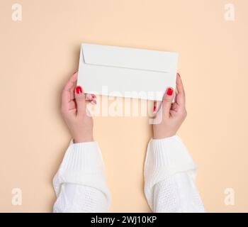 Zwei weibliche Hände halten einen weißen rechteckigen Umschlag auf beigefarbenem Hintergrund, Draufsicht Stockfoto