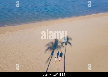 Blick von oben auf die Drohne auf ein paar Männer und Frauen, die mit Palmen am Strand spazieren gehen Stockfoto