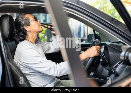 Betrunkener asiatischer junger Mann fährt ein Auto mit einer Flasche Bier, gefährliches Fahrkonzept. Stockfoto