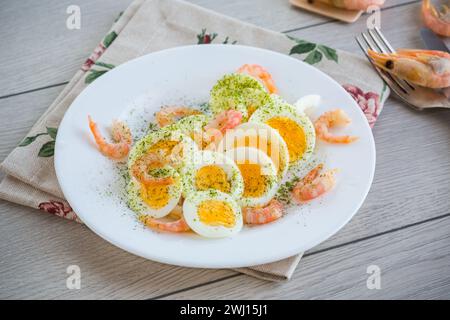 Gekochte Eier mit gekochten Garnelen auf einem Teller zum Frühstück, auf einem Holzbrett Stockfoto