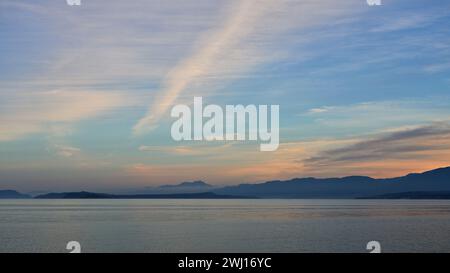 Dramatischer Himmel über dem Meer bei Sonnenuntergang mit der Silhouette entfernter Berge. Stockfoto