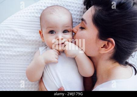 Die schöne junge Mutter küsst ihr süßes Baby auf die Wange. Weißliche Brünette berührt ihr lächelndes Kind mit ihrem Gesicht. Stockfoto