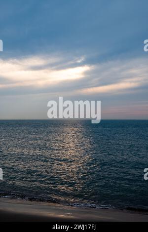 Dieses ruhige Bild fängt die ruhige Schönheit des Meeres ein, während der Tag in Richtung Abend übergeht. Sonnenstrahlen brechen durch den bewölkten Himmel und werfen ein weiches, diffuses Licht über die Wasseroberfläche und erzeugen eine friedliche und besinnliche Stimmung. Die Horizontlinie, an der das dunkelblaue Meer auf den Himmel trifft, ist klar und beruhigend, während die sanften Wellen in der Nähe der Küste sanft am Strand liegen. Diese Meereslandschaft ist ein Beweis für die ruhigen Momente der Natur, die zum Nachdenken und zur Ruhe einladen. Ruhige Meereslandschaft mit Sonnenstrahlen, die durch Wolken durchdringen. Hochwertige Fotos Stockfoto