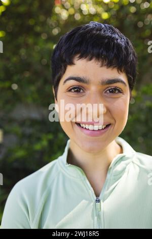 Porträt einer glücklichen birassischen Frau mit kurzen dunklen Haaren, die im sonnigen Garten lächelt Stockfoto