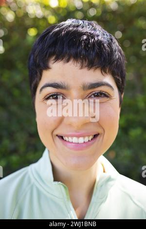 Portrait Nahaufnahme einer glücklichen birassischen Frau mit kurzen dunklen Haaren, die im sonnigen Garten lächelt Stockfoto