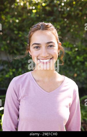 Porträt einer glücklichen Frau mit langen braunen Haaren, die im sonnigen Garten lächelt Stockfoto