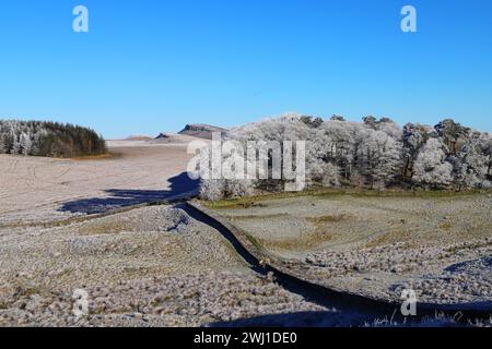 Abschnitt der Hadriansmauer in der Nähe des römischen Forts Housesteads mit Whin Sill im Hintergrund an einem frostigen Tag im Januar 2024. Stockfoto