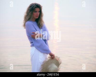 Junge blonde Frau, die bei Sonnenuntergang am Wasser steht. Stockfoto