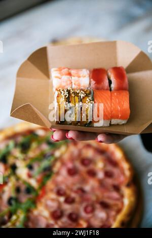 Sushi-Set auf Packschachtel in der Hand auf Pizza Hintergrund. Street Food Stockfoto