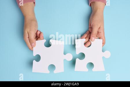 Weibliche Hand hält zwei große leere weiße Puzzles auf blauem Hintergrund Stockfoto