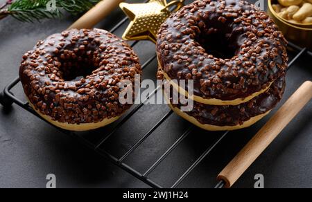 Schokoladen-Donuts, bestreut mit zerquetschten Nüssen auf einem schwarzen Tisch Stockfoto