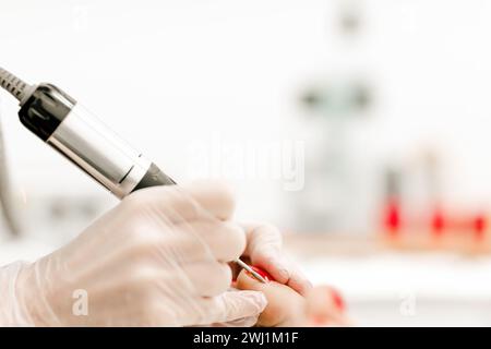 Nahaufnahme der Füße einer Frau während einer Pediküre, Auftragen von leuchtendem rotem nagellack und Hervorhebung detaillierter Nagelpflege- und Schönheitsroutine Stockfoto