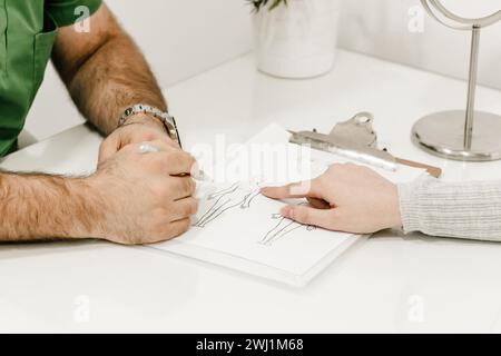 Nahaufnahme der Hand einer Frau, die auf ein Dokument zeigt, in einem Gespräch mit einem männlichen Schönheitschirurgen, mit Schwerpunkt auf ärztlicher Beratung Stockfoto