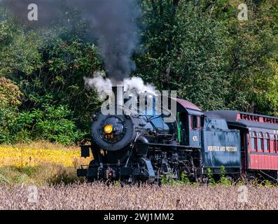 Ansicht einer restaurierten Dampflok, die Passagierbusse zieht und an einem Herbsttag Rauch bläst Stockfoto