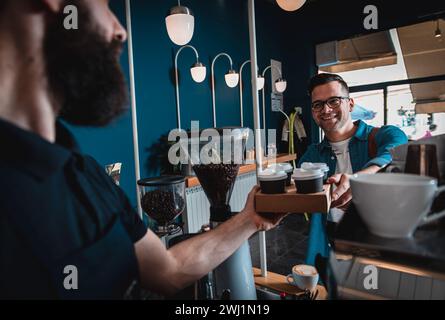 Männer im Coffee Shop kaufen Cappuccino in Plastikbecher und bezahlen mit Karte. Stockfoto