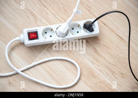 Elektrischer Stecker und Mehrfachsteckdose auf dem Boden, Nahaufnahme. Stockfoto